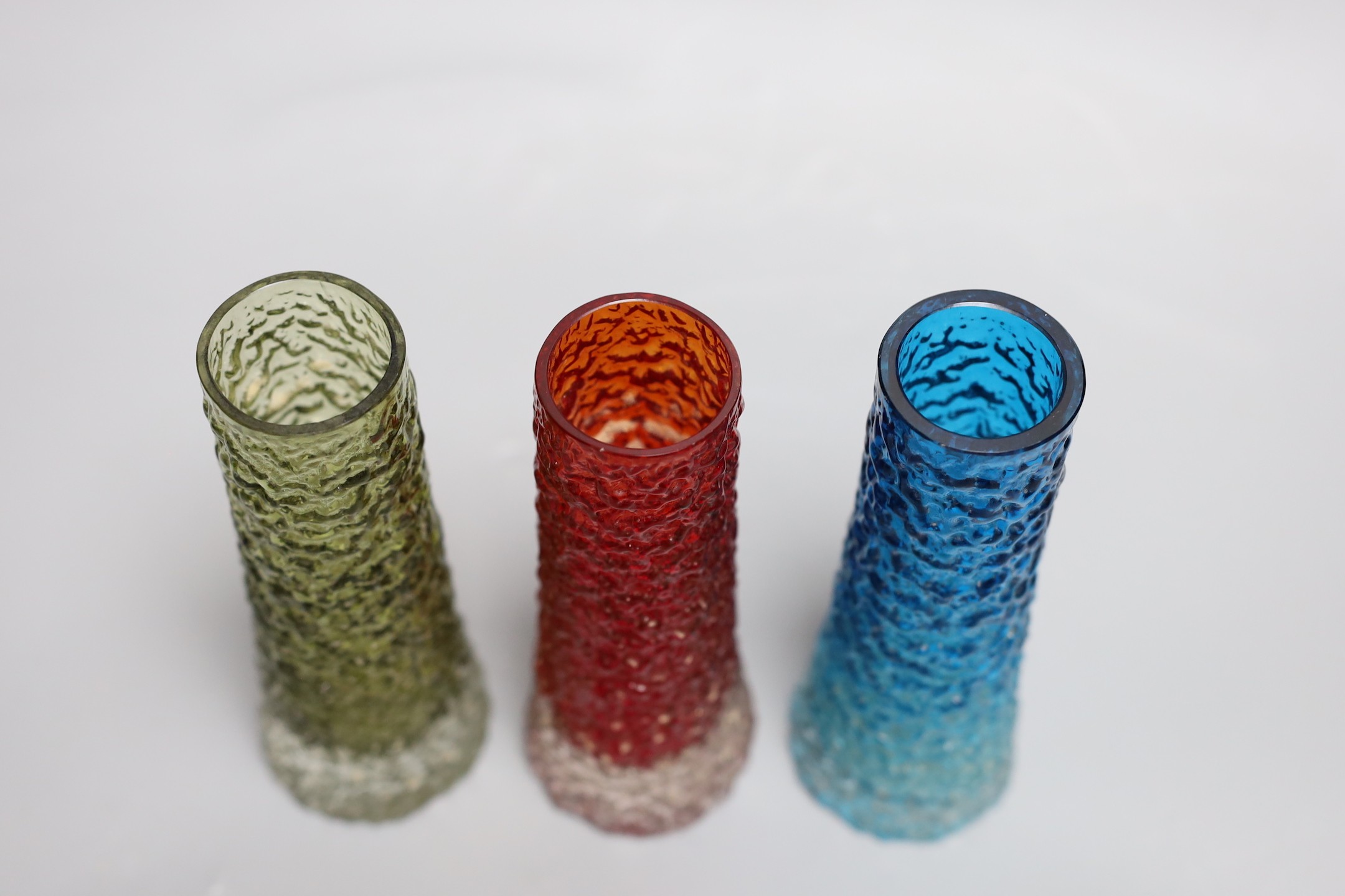 A trio of tapering 'bark' Whitefriar vases, model 9729 designed by Geoffrey Baxter, in red, kingfisher blue and sage green glass, each 16cm high.